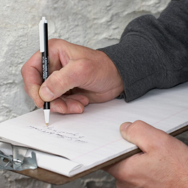 A professional writing on a clipboard as he inspects a home's stucco siding