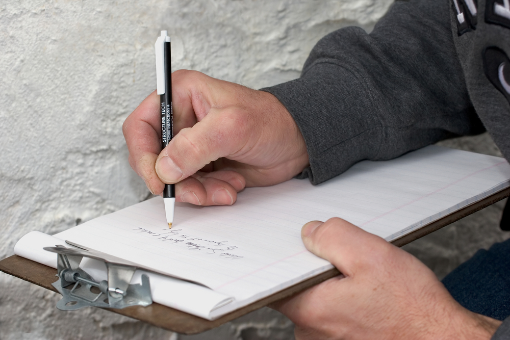 A professional writing on a clipboard as he inspects a home's stucco siding